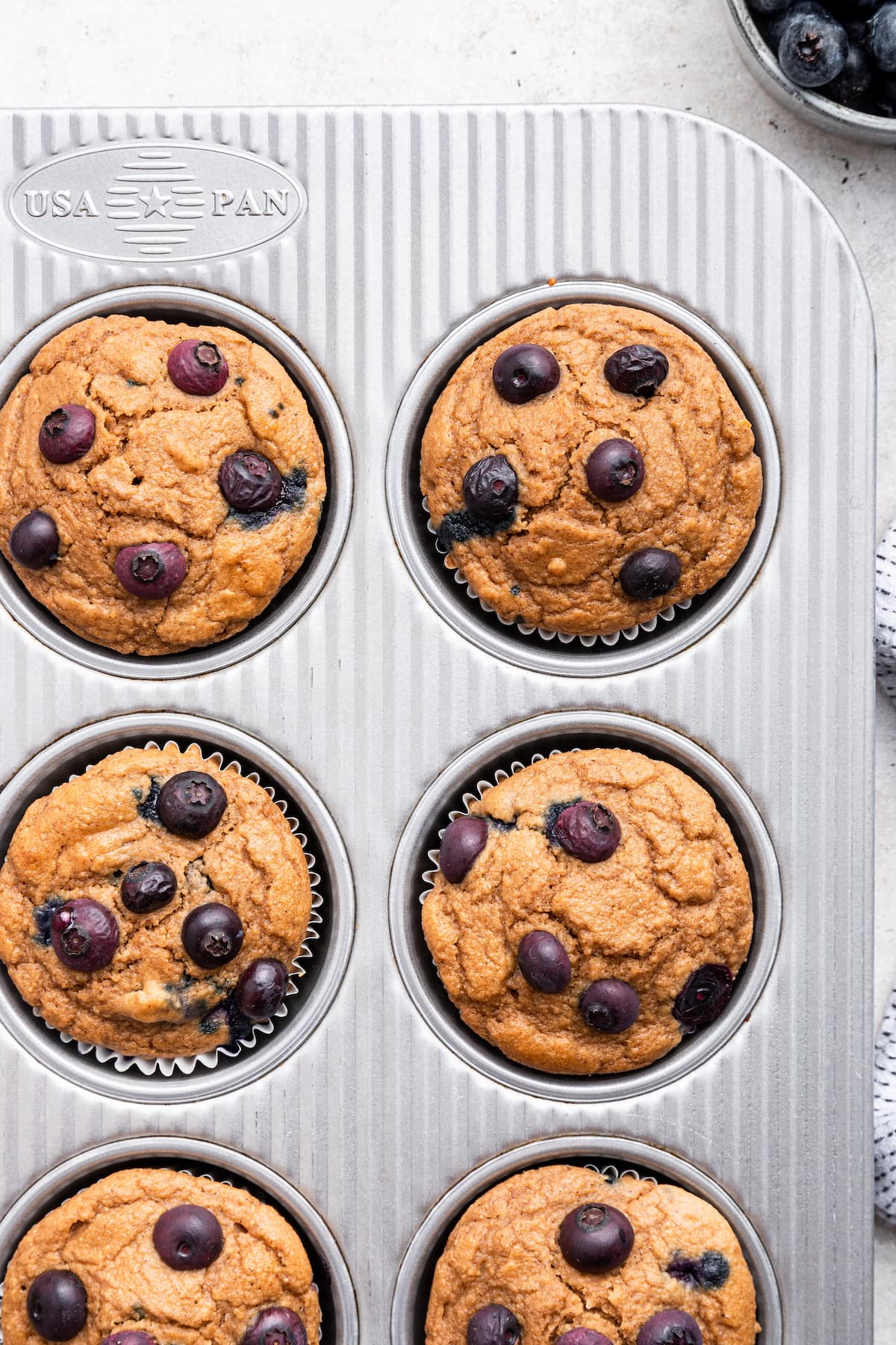 Multiple blueberry protein muffins in a muffin tin.