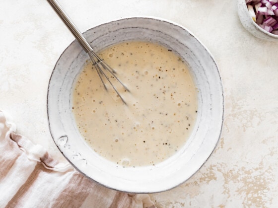 A yogurt and apple cider vinegar mixture in a mixing bowl with a metal whisk.