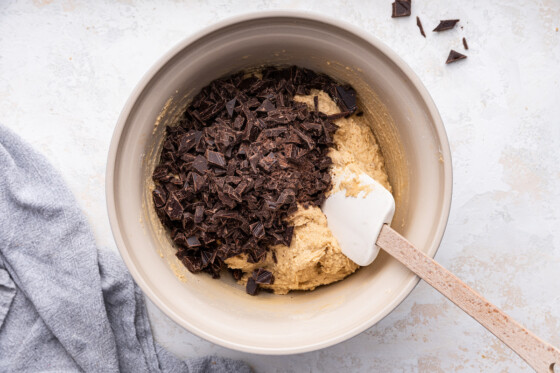 Chocolate chunks added to the cookie dough in a large mixing bowl.