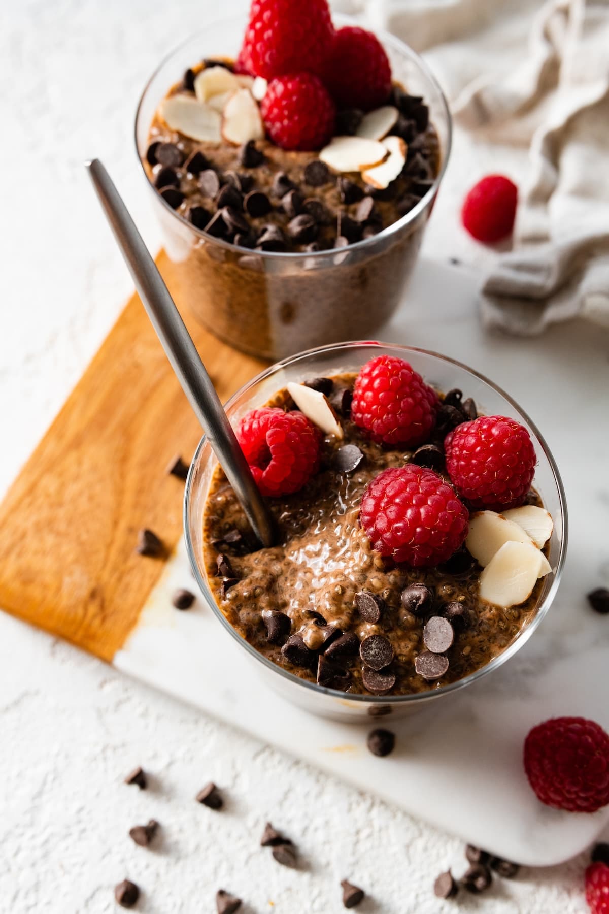 A chocolate chia pudding in a glass cup topped with chocolate chips, sliced almonds, and fresh raspberries.