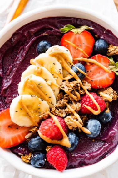 An acai bowl topped with fresh berries, sliced banana, granola, and a drizzle of nut butter.