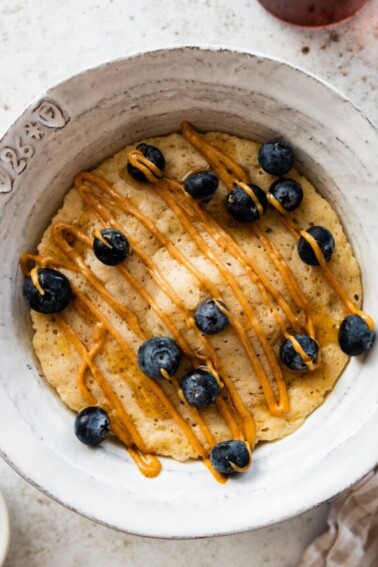 A protein pancake in a bowl topped with a drizzle of peanut butter and fresh blueberries.