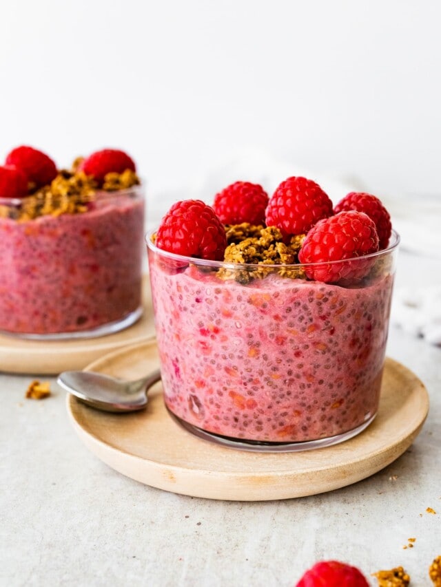 A raspberry chia pudding in a glass cup, topped with fresh raspberries and granola.