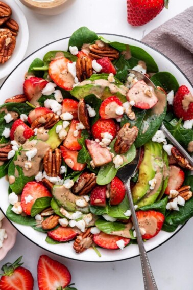 Strawberry spinach salad in a serving bowl drizzled with creamy balsamic dressing and served with serving spoons.