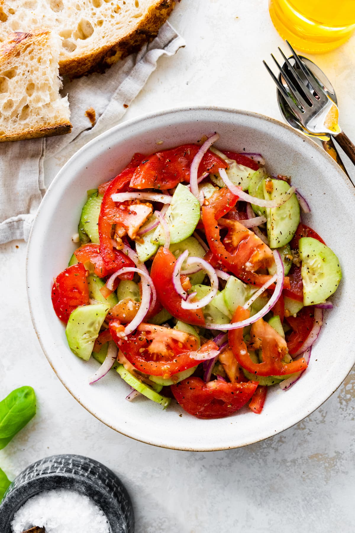 In a small white bowl, a cucumber tomato salad with sliced red onion, salt, and pepper.