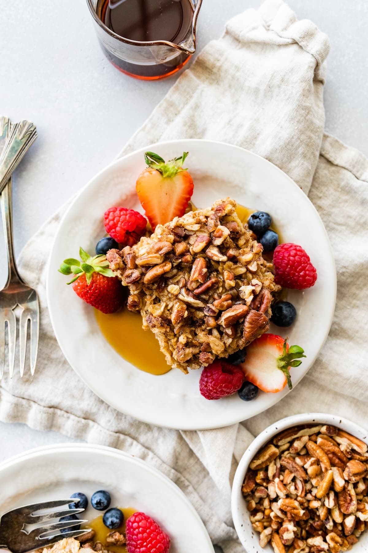 A slice of baked oatmeal served on a white plate with maple syrup and fresh berries.