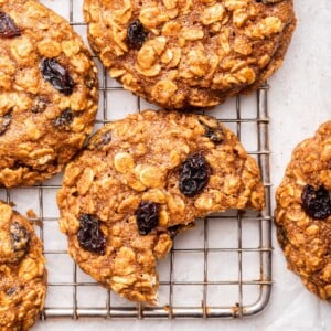 Oatmeal raisin cookies on a cooling rack with one cookie having a bite taken from it.
