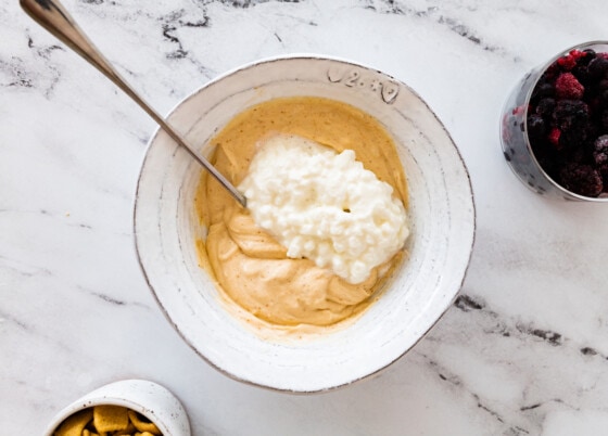 Cottage cheese added to a peanut butter yogurt mixture in a bowl.