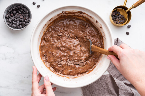 Wet and dry ingredients being combined with a silicone spatula in a large mixing bowl.
