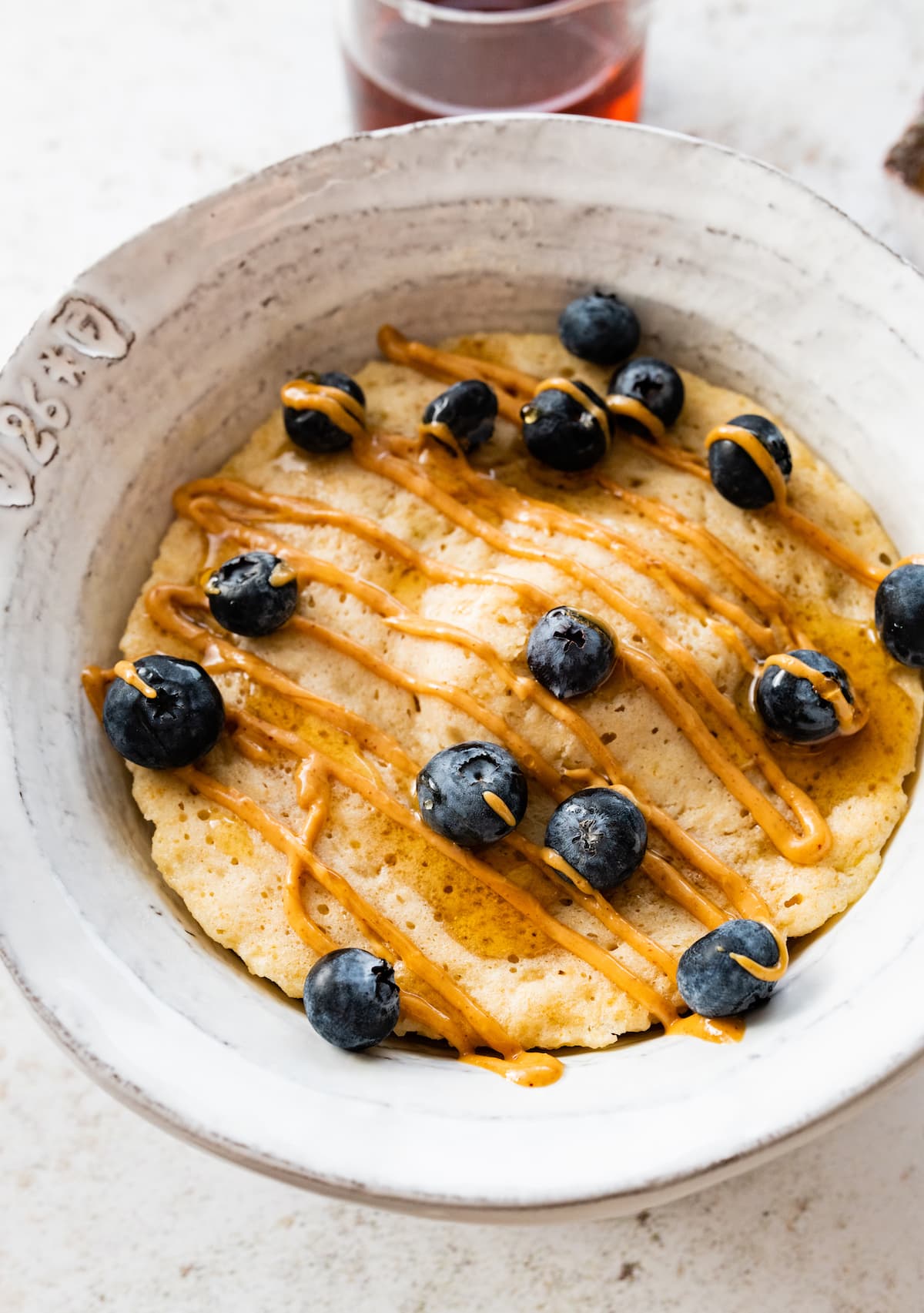 A protein pancake in a bowl topped with a drizzle of peanut butter and fresh blueberries.