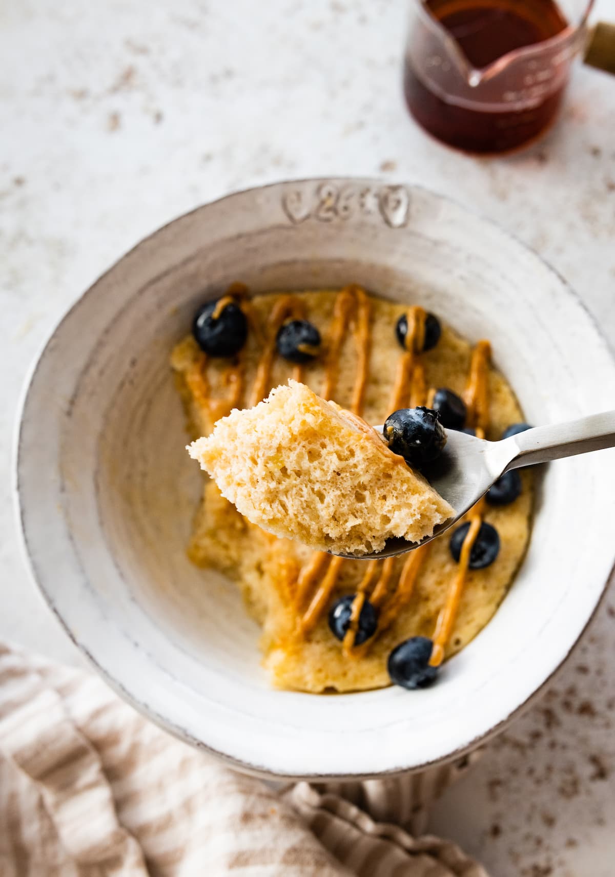 A bite size portion of a protein pancake on a spoon just above a bowl of the pancake.