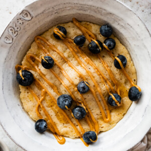 A protein pancake in a bowl topped with a drizzle of peanut butter and fresh blueberries.