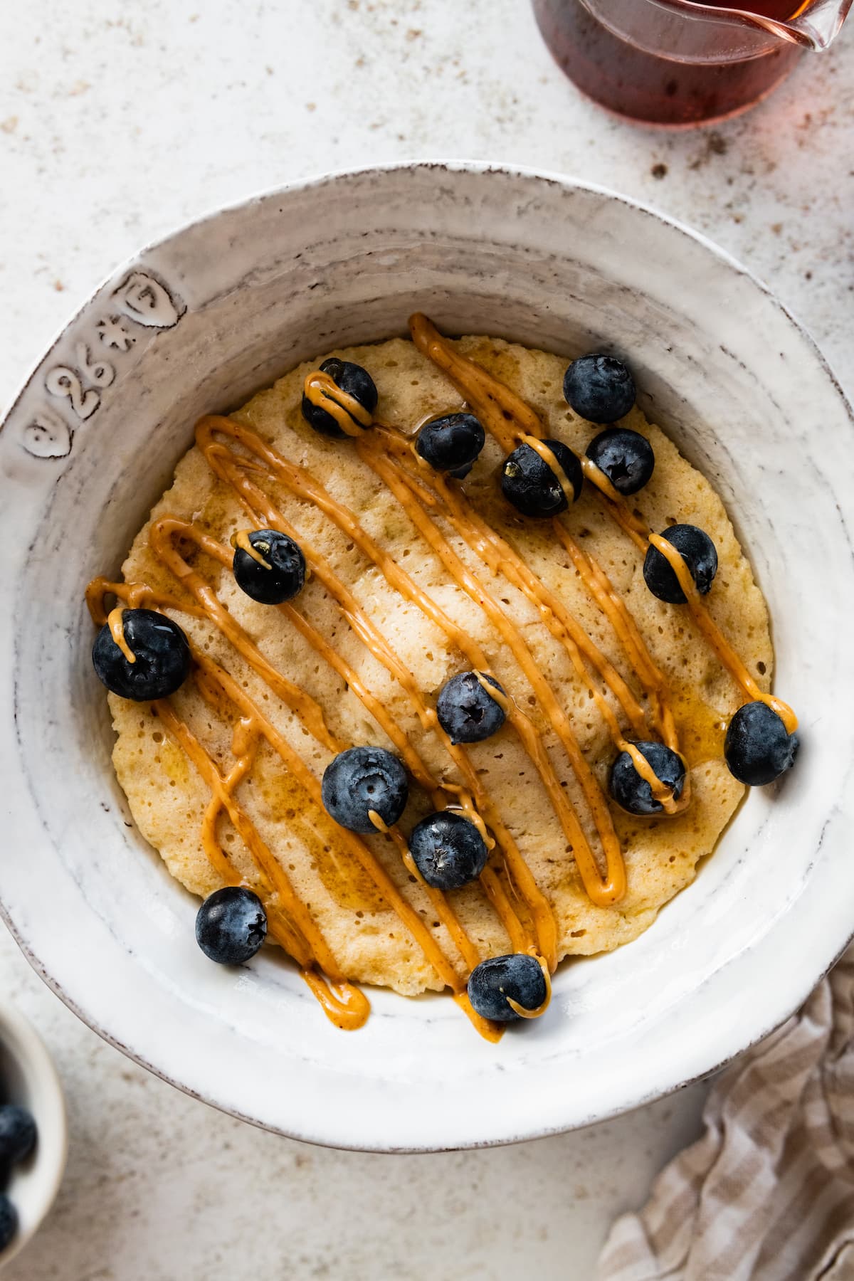 A protein pancake in a bowl topped with a drizzle of peanut butter and fresh blueberries.