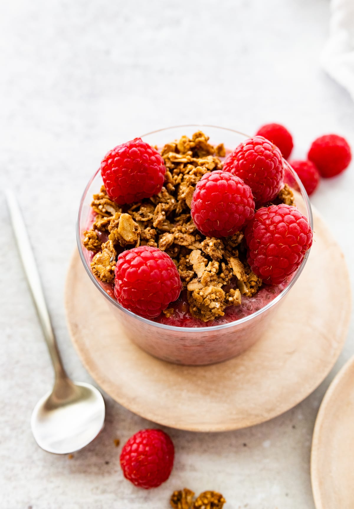 A raspberry chia pudding in a glass cup, topped with fresh raspberries and granola.