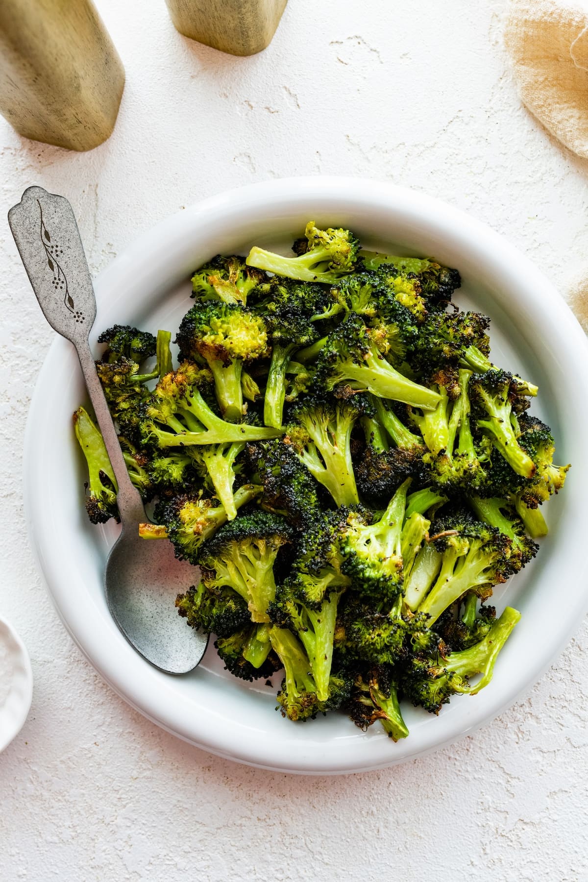 Roasted broccoli on a white plate with a serving spoon.