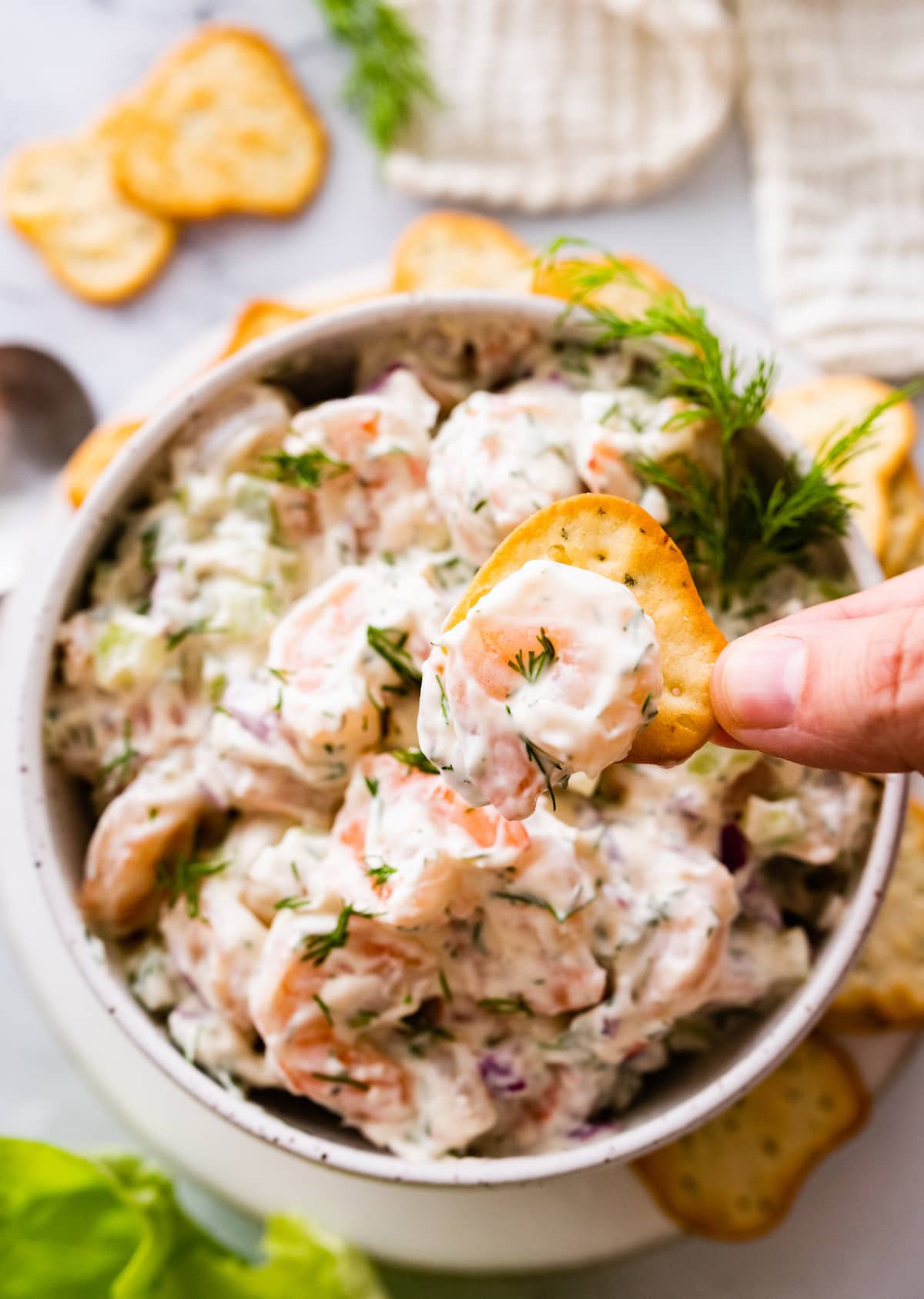 A woman's hand scooping up shrimp salad with a cracker.