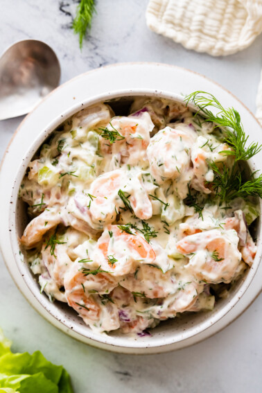 Shrimp salad in a serving bowl topped with fresh dill.