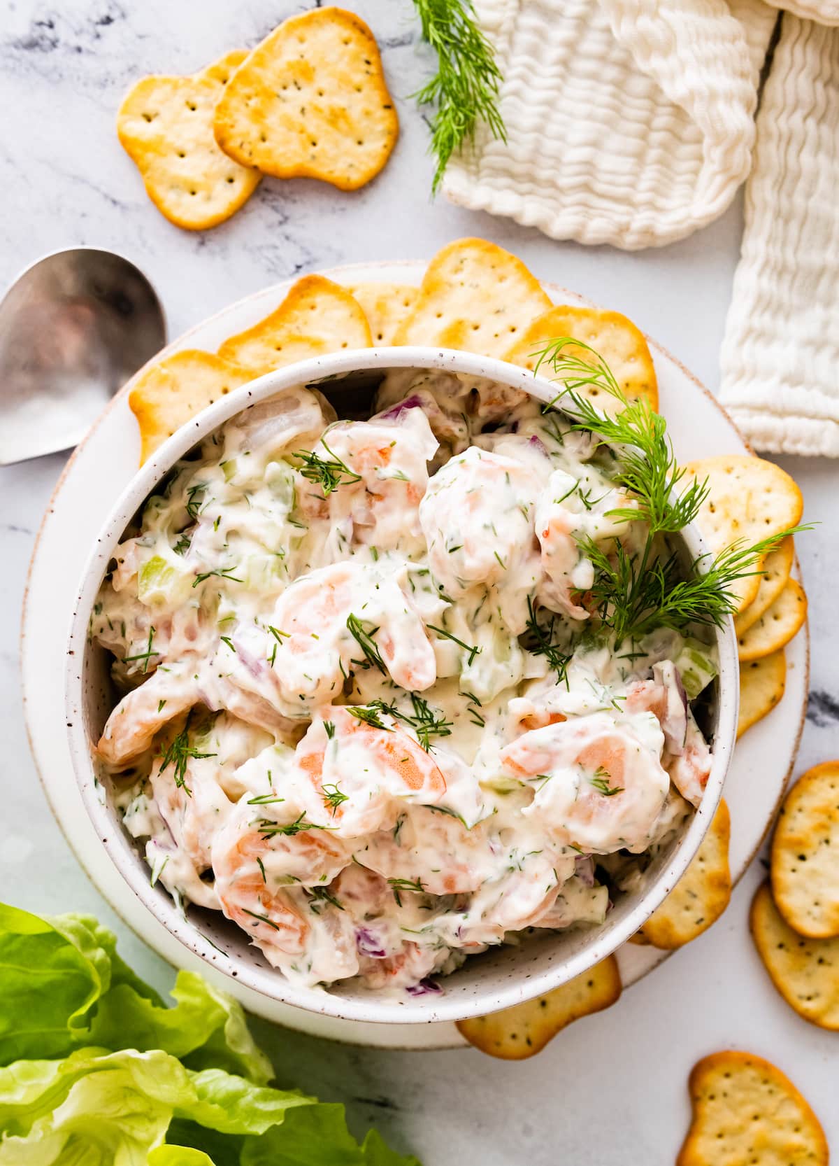 Shrimp salad in a serving bowl topped with fresh dill and served with crackers on the side.