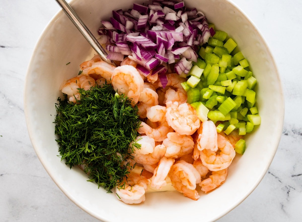 Ingredients for the shrimp salad in a white mixing bowl.