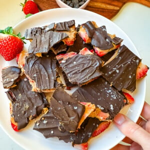 Chocolate strawberry bark on a pink plate held by a woman's hand.