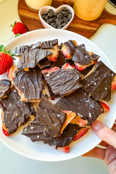 Chocolate strawberry bark on a pink plate held by a woman's hand.