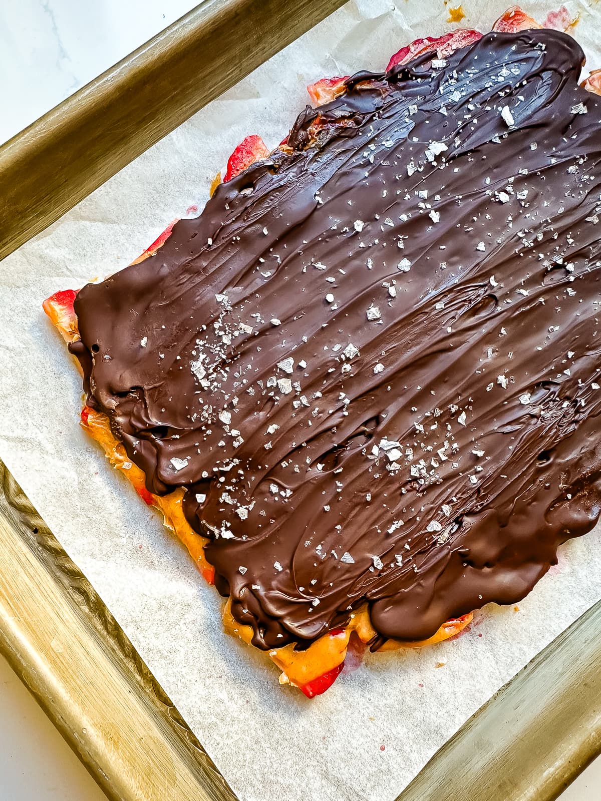 A sheet pan lined with parchment with strawberry peanut butter chocolate bark on top.