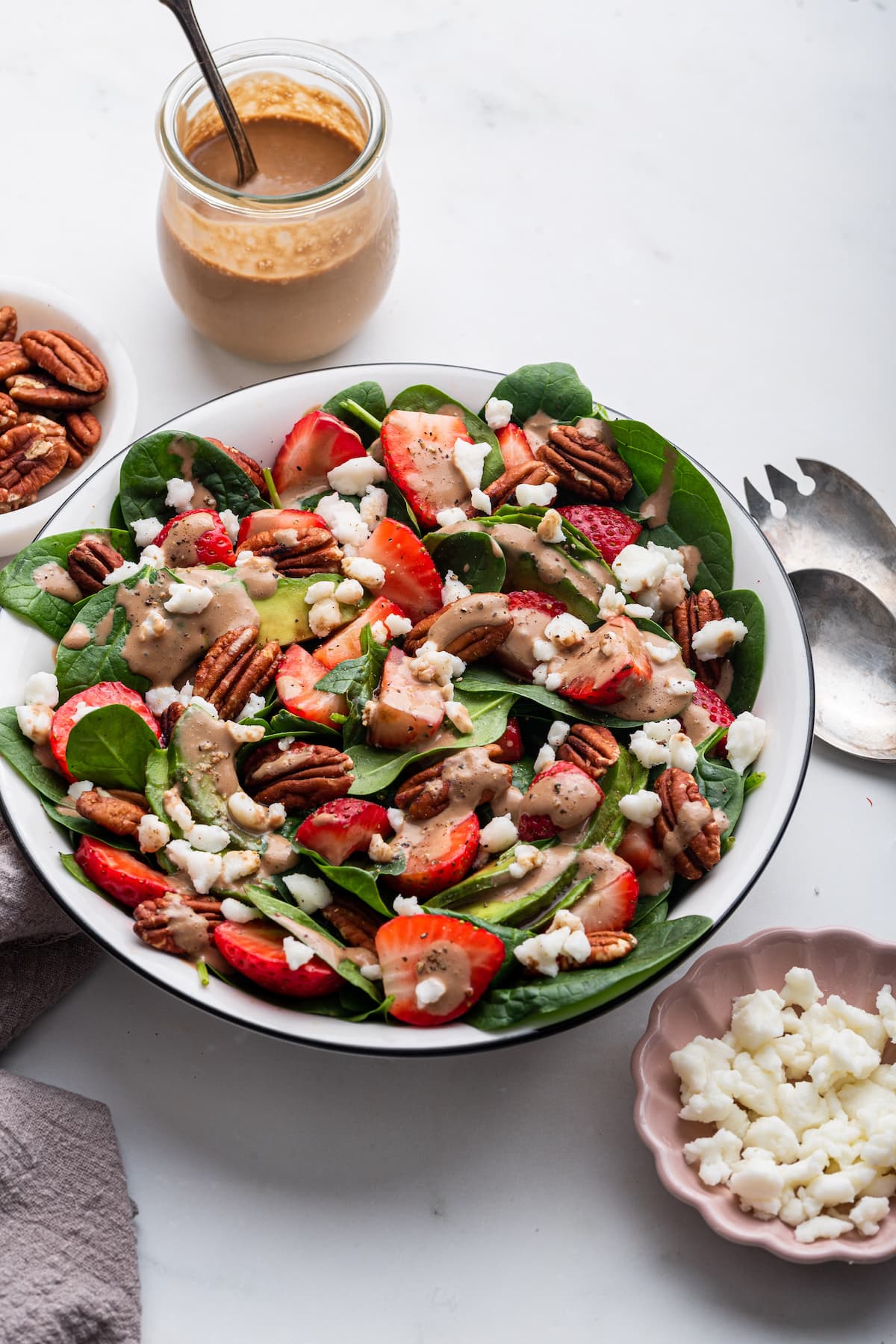Strawberry spinach salad in a serving bowl drizzled with creamy balsamic dressing.
