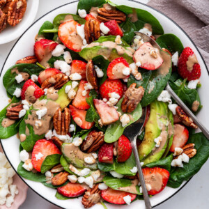 Strawberry spinach salad in a serving bowl drizzled with creamy balsamic dressing and served with serving spoons.