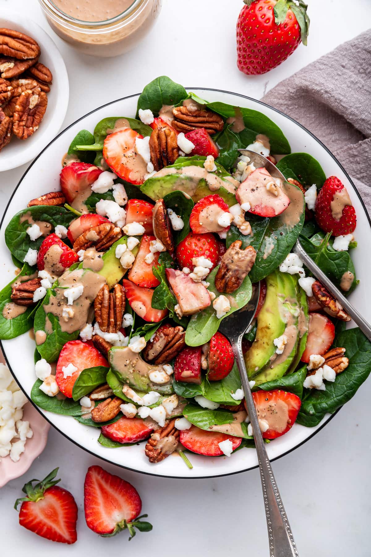 Strawberry spinach salad in a serving bowl drizzled with creamy balsamic dressing and served with serving spoons.