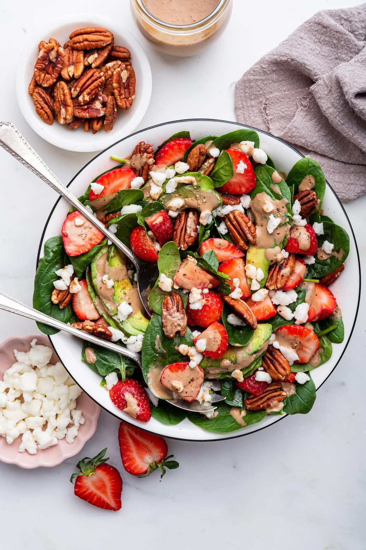 Strawberry spinach salad in a serving bowl with serving spoons.
