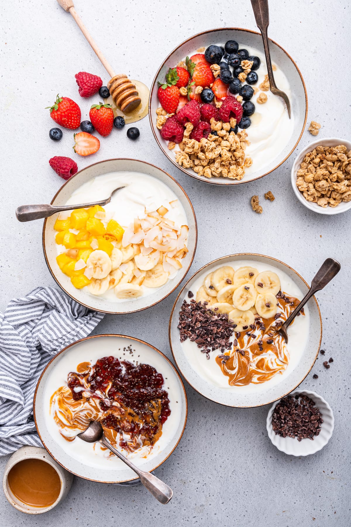 Four yogurt bowls served in white bowls with spoons.