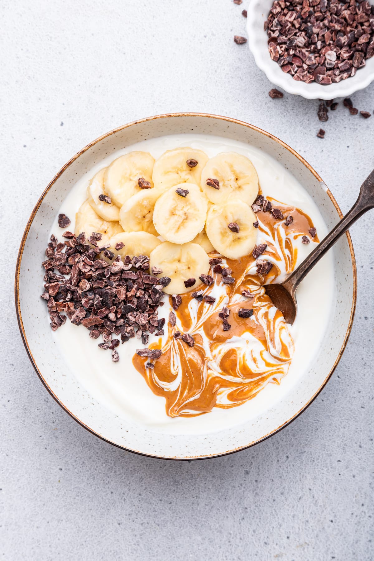 A chunky monkey yogurt bowl topped with peanut butter, cacao nibs and fresh banana slices.