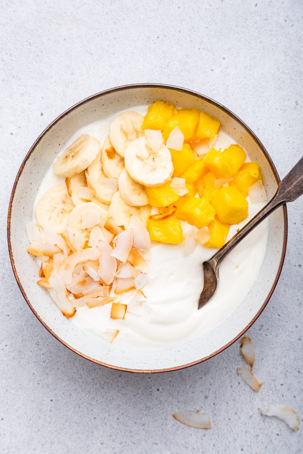 A yogurt bowl topped with fresh banana, mango and toasted coconut.