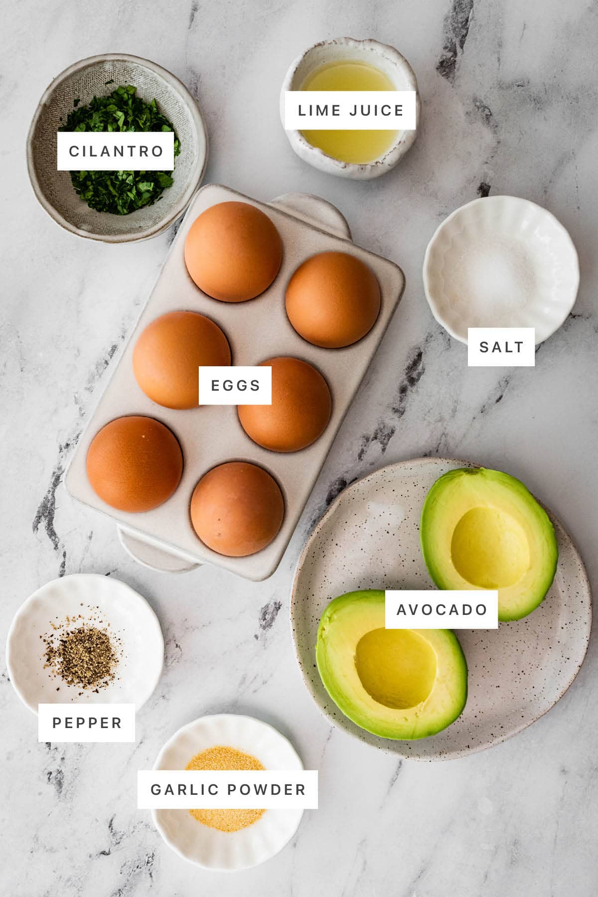 Ingredients measured out to make Avocado Deviled Eggs: cilantro, lime juice, salt, eggs, pepper, garlic powder and avocado.