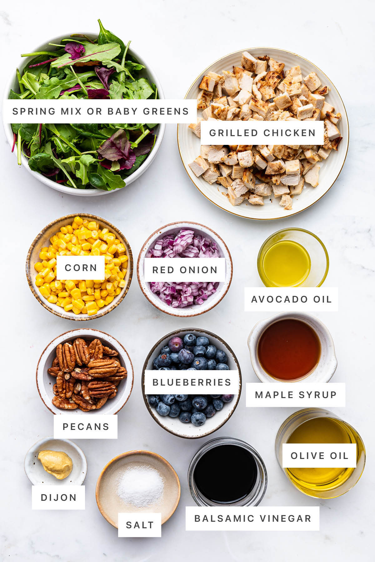 Ingredients measured out to make Blueberry Corn Chicken Salad: spring mix, grilled chicken, corn, red onion, avocado oil, pecans, blueberries, maple syrup, dijon, salt, balsamic vinegar and olive oil.