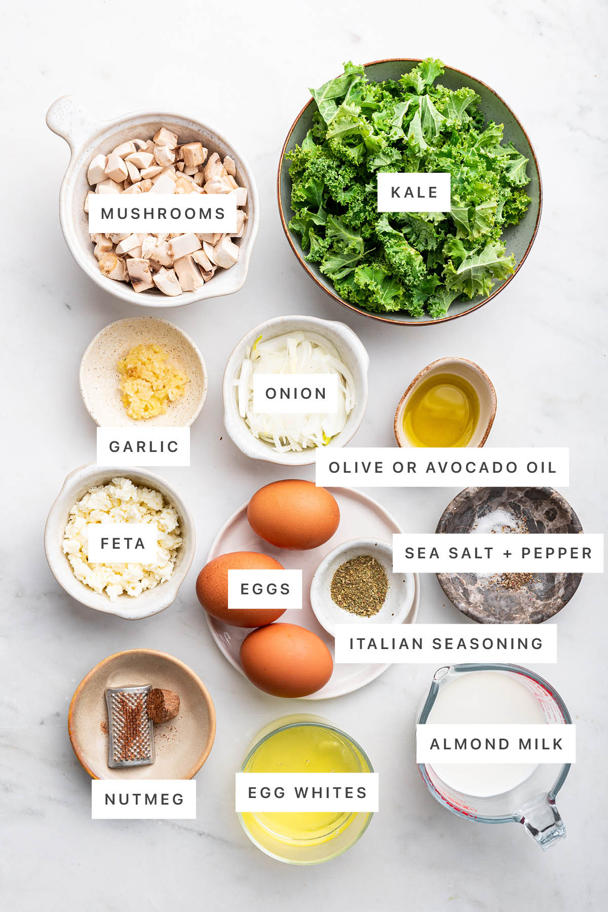 Ingredients measured out to make Kale and Feta Crustless Quiche: mushrooms, kale, garlic, onion, oil, feta, eggs, salt, pepper, Italian seasoning, nutmeg, egg whites and almond milk.