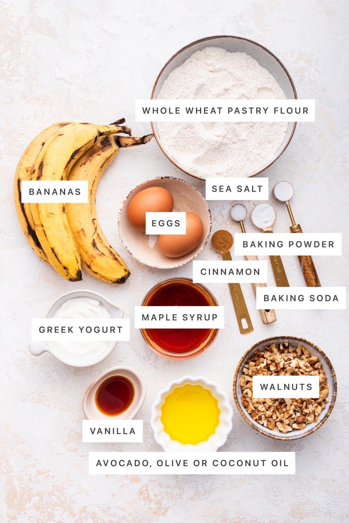 Ingredients measured out to make Healthy Banana Muffins: whole wheat flour, bananas, eggs, sea salt, cinnamon, baking powder, baking soda, maple syrup, Greek yogurt, vanilla, oil and walnuts.