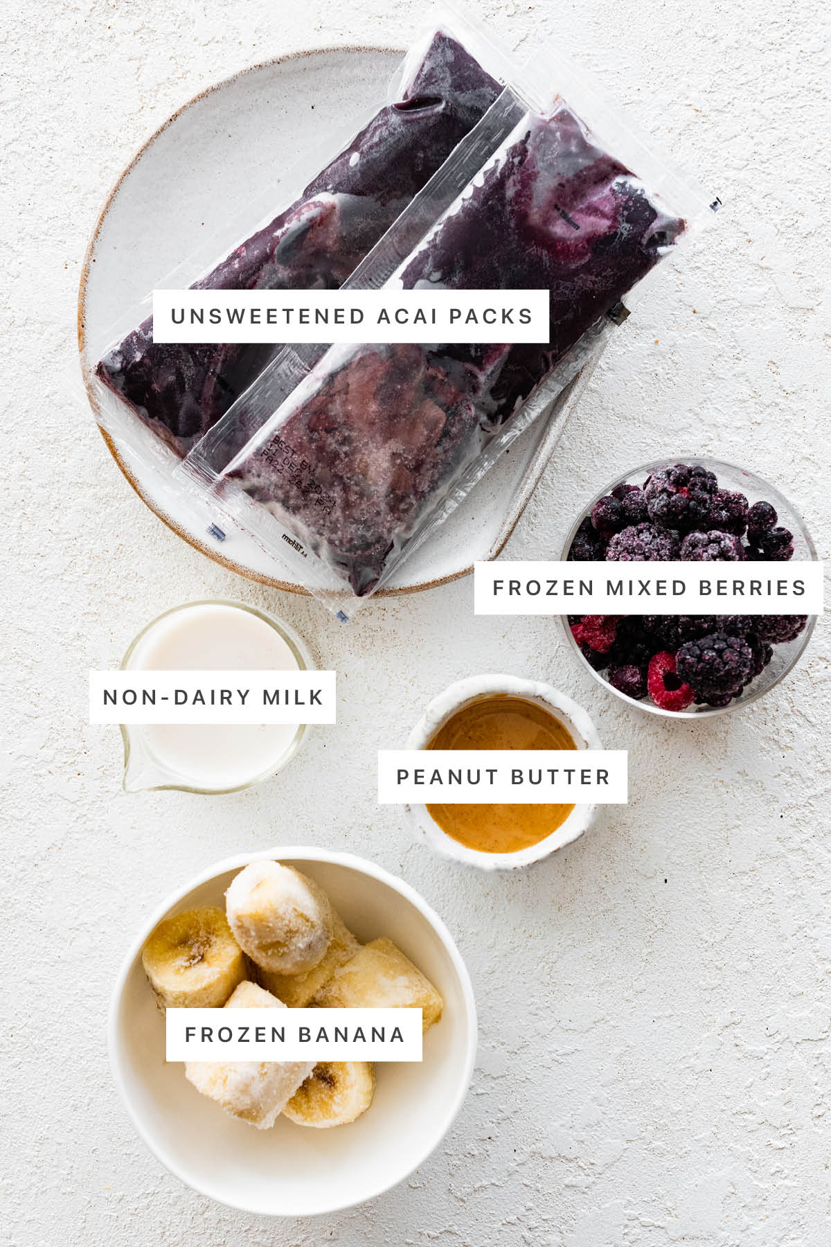 Ingredients measured out to make an acai bowl: unsweetened acai packs, frozen mixed berries, non-dairy milk, peanut butter, frozen banana.