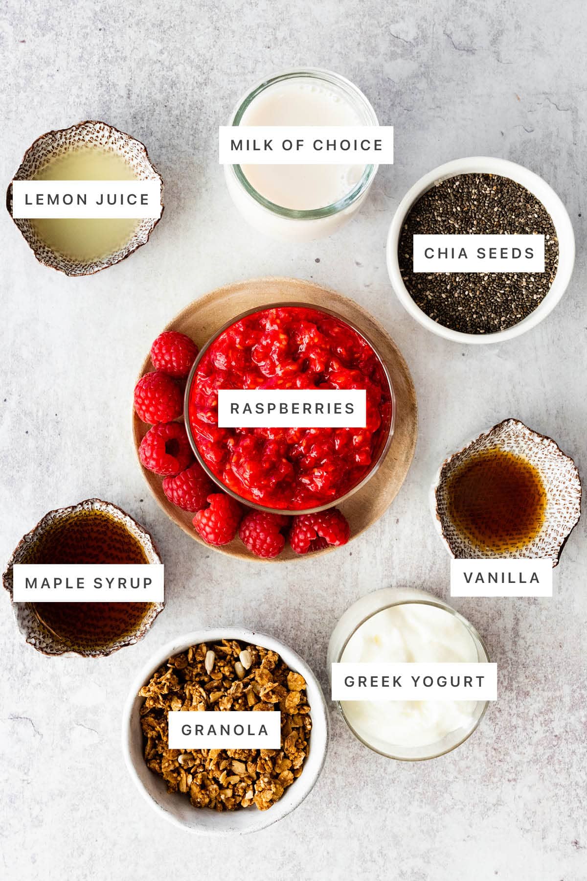Ingredients measured out to make Raspberry Chia Pudding: lemon juice, milk, chia seeds, raspberries, vanilla, maple syrup, granola and Greek yogurt.