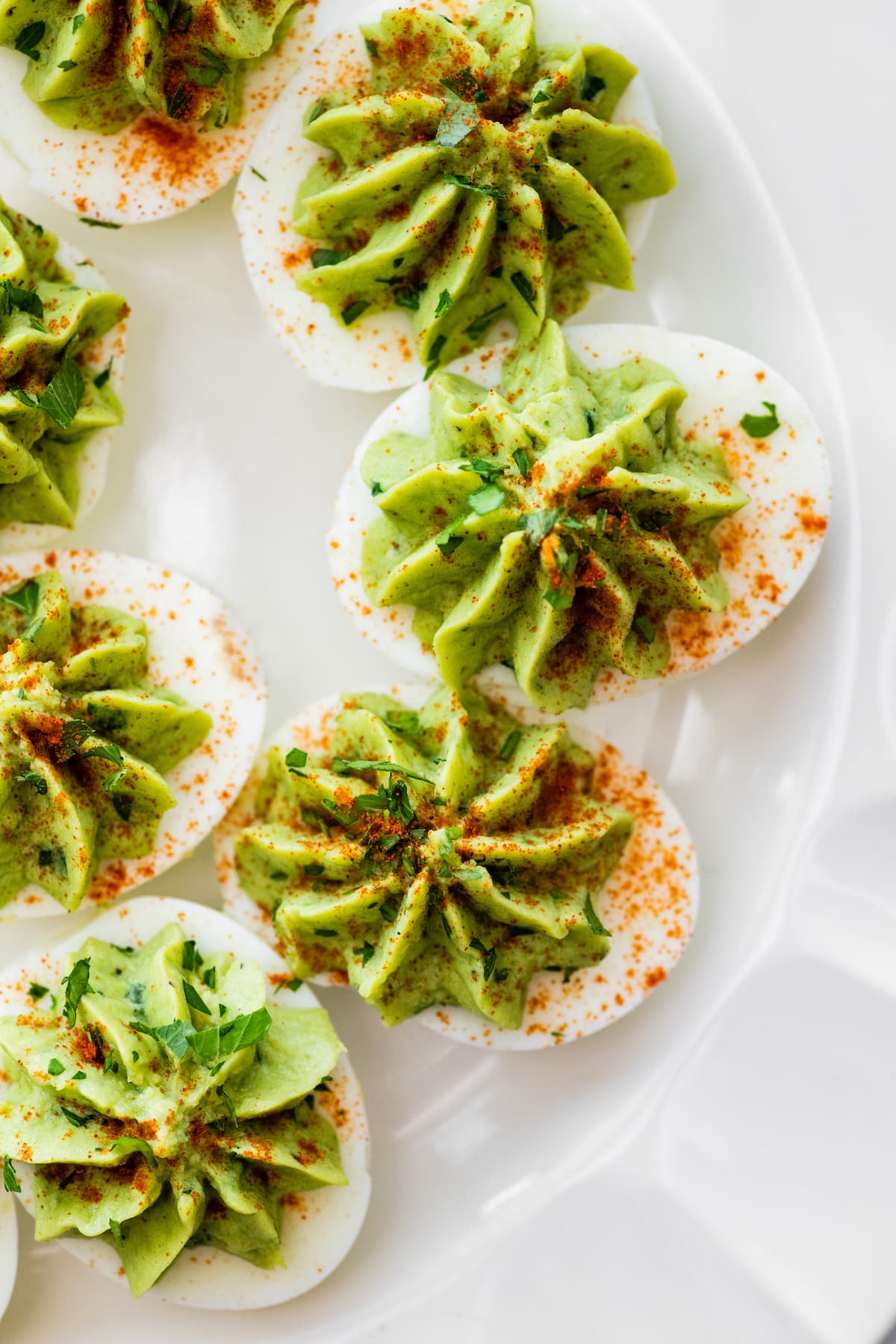 Avocado deviled eggs near one another on a plate and topped with a dash of paprika and fresh herbs.