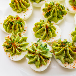 Avocado deviled eggs near one another on a plate and topped with a dash of paprika and fresh herbs.