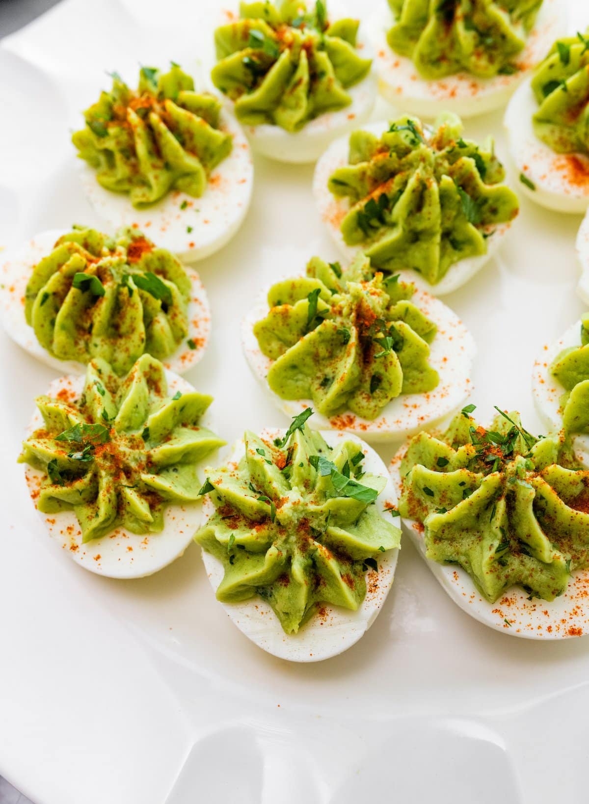 Avocado deviled eggs near one another on a plate and topped with a dash of paprika and fresh herbs.