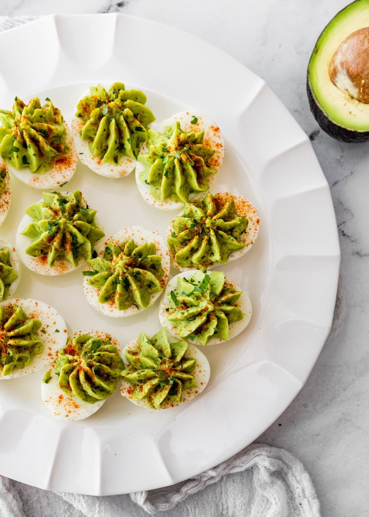 Avocado deviled eggs near one another on a plate and topped with a dash of paprika and fresh herbs.