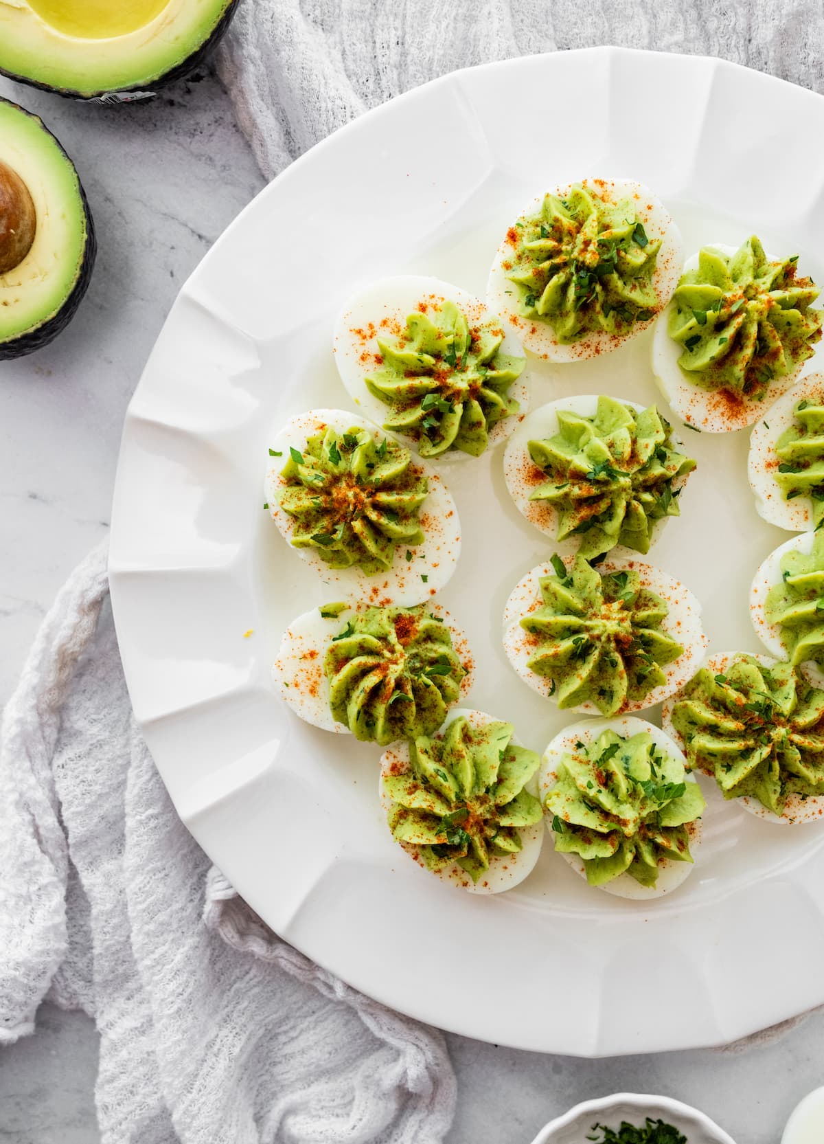 Avocado deviled eggs near one another on a plate and topped with a dash of paprika and fresh herbs.