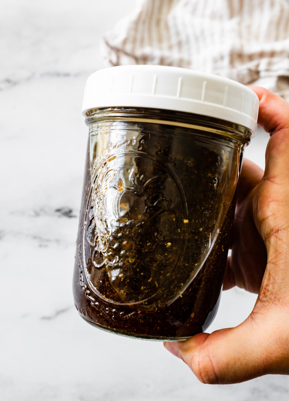 A hand holding a jar of balsamic vinaigrette.