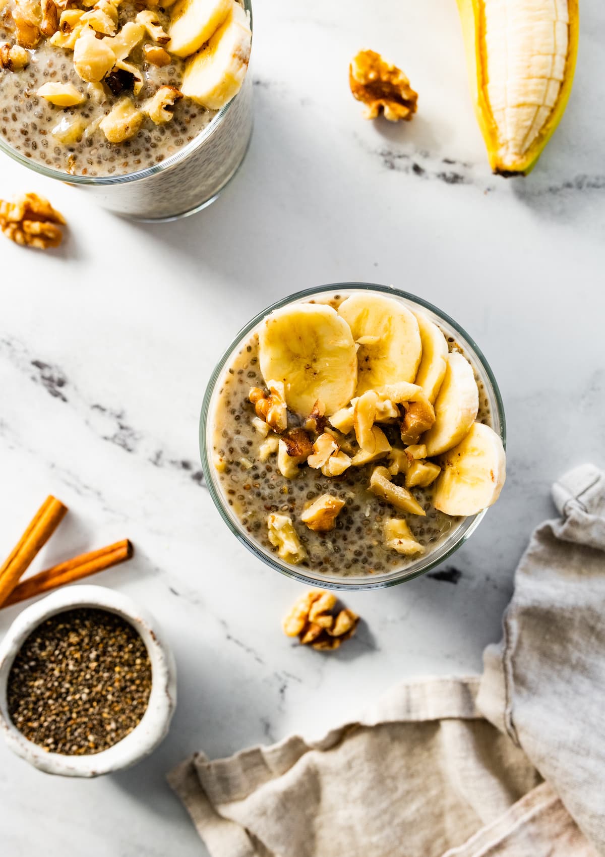 Banana chia pudding in a glass cup, topped with banana slices and walnuts.