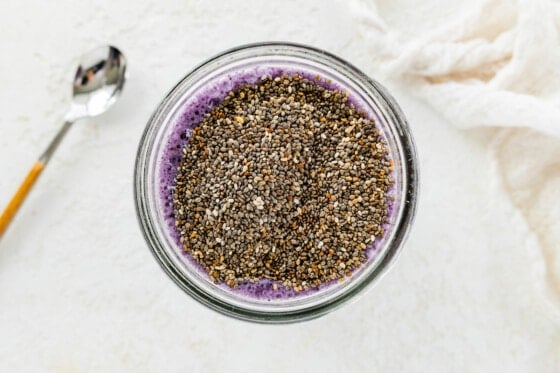 Chia seeds added to a mason jar of a blueberry milk mixture.