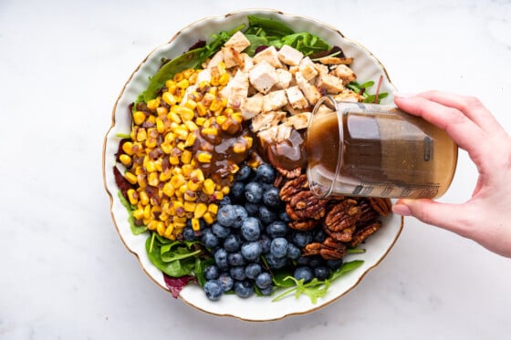 A woman's hand pouring dressing on blueberry corn chicken salad.