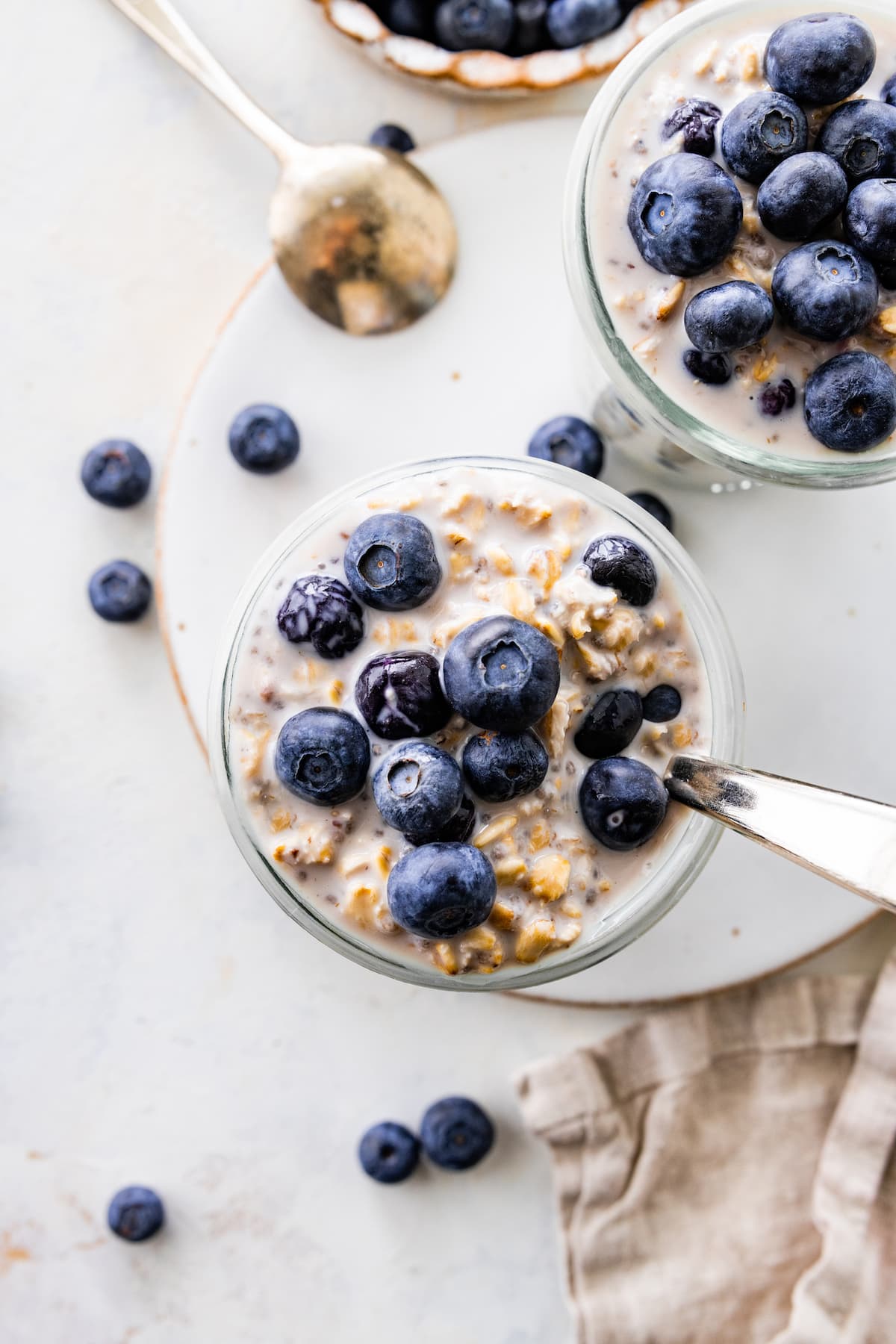 Two glasses of blueberry overnight oats topped with fresh blueberries.