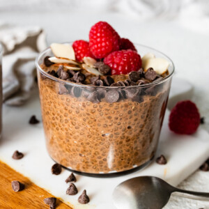 A chocolate chia pudding in a glass cup topped with chocolate chips, sliced almonds, and fresh raspberries.